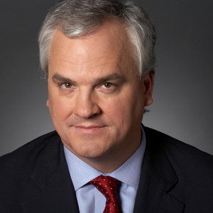 A headshot of a man in a business suit and a red tie with a slight smile on his face.