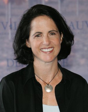 A headshot of a smiling, dark-haired woman, wearing a dark shirt and a necklace.